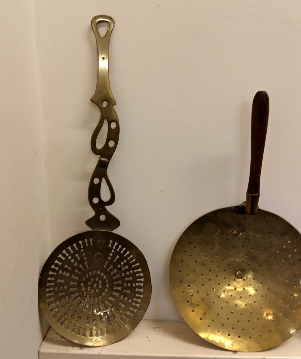 A collection of four antique brass cream skimmers with pierced round bowls, featuring turned wooden handles and decorative flat brass handles. View IV