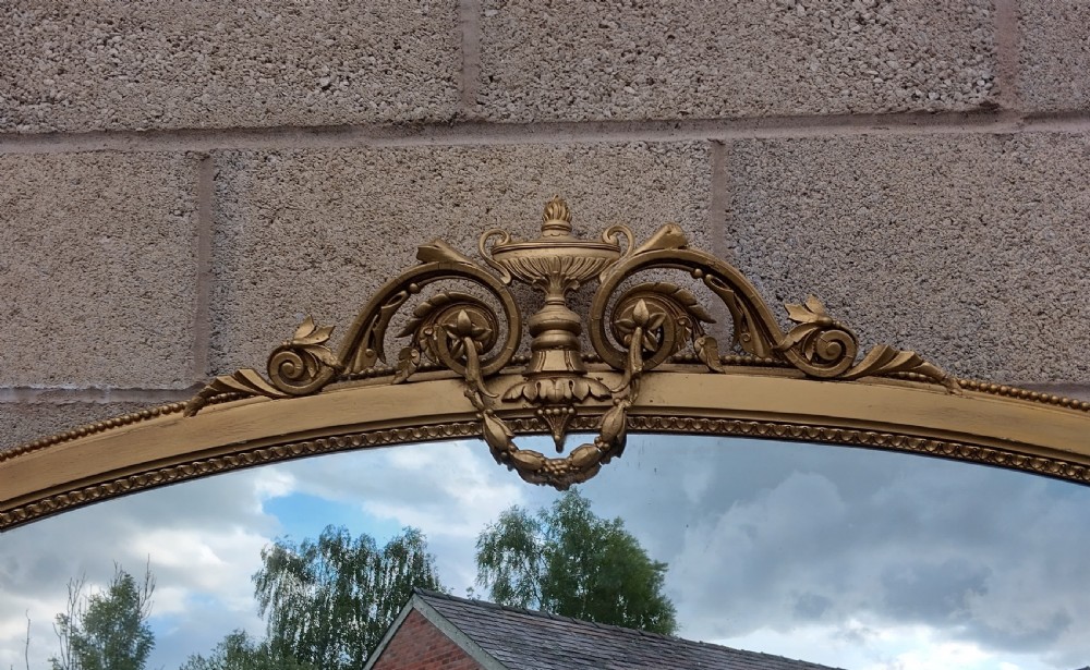 A 19th-century arched gilt overmantel mirror featuring an ornate top crest with an urn and scrollwork motifs. View VII