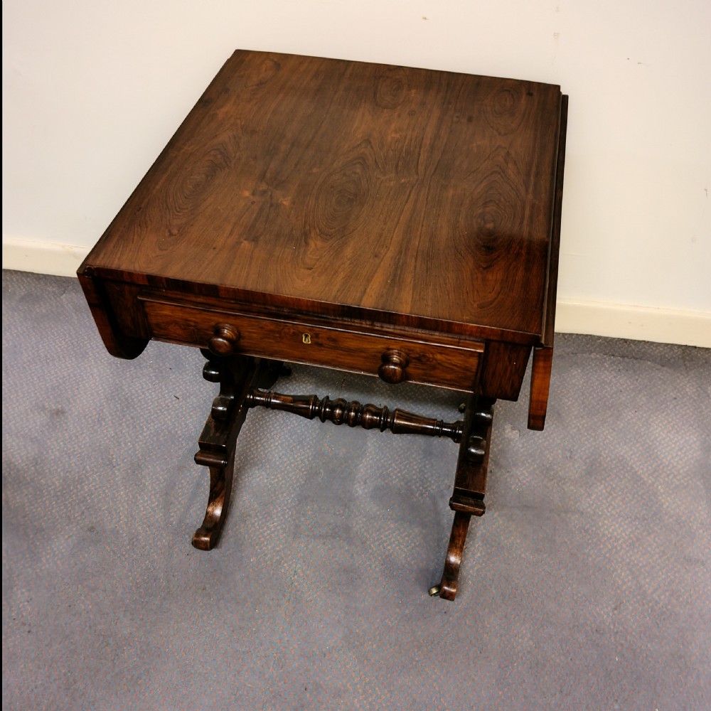 A 19th-century dark rosewood drop-leaf occasional table featuring a single drawer with wooden knobs, resting on curved trestle legs connected by a turned stretcher. View V
