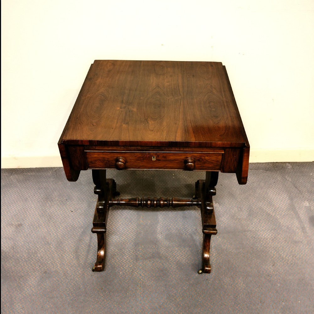 A 19th-century dark rosewood drop-leaf occasional table featuring a single drawer with wooden knobs, resting on curved trestle legs connected by a turned stretcher. View VI