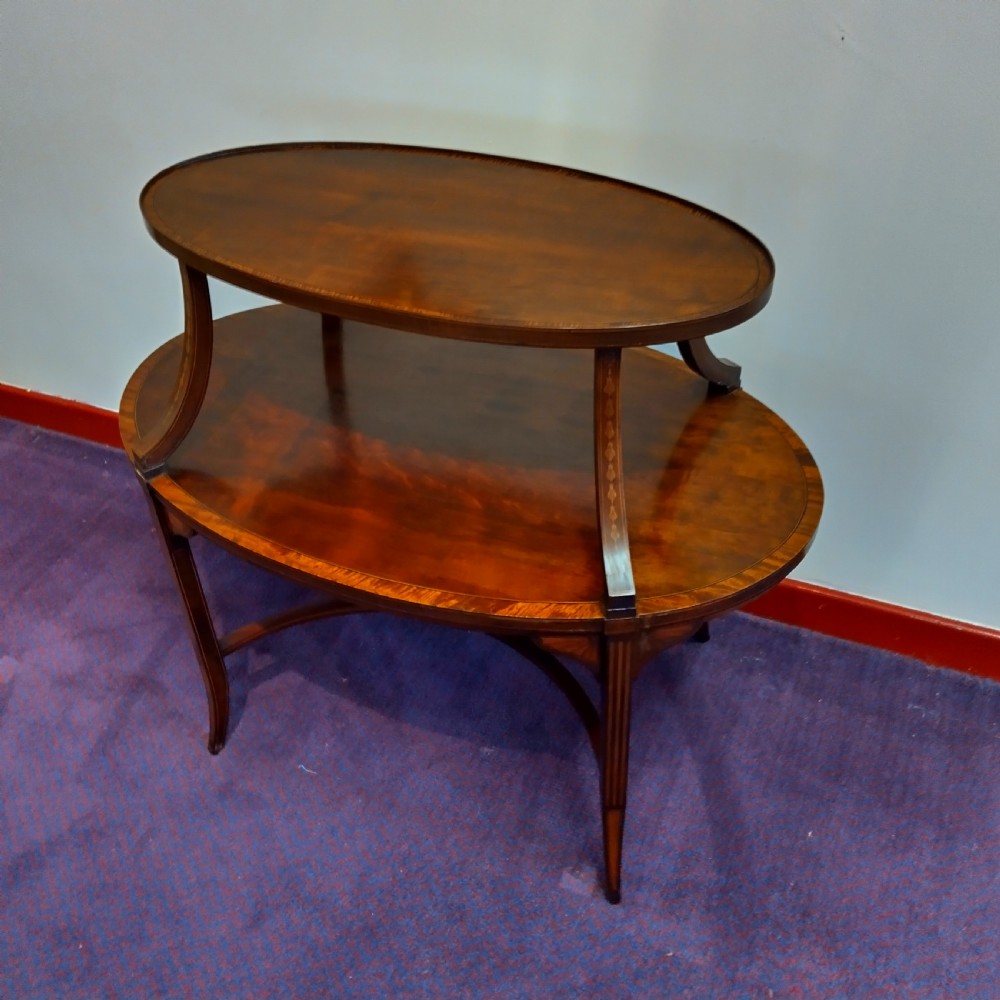 An Edwardian oval mahogany occasional table featuring two tiered surfaces connected by curved supports and decorated with delicate inlay stringing.