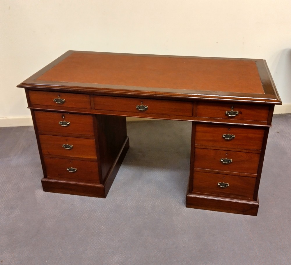 An Edwardian mahogany pedestal desk featuring a brown leather inset writing surface, nine drawers, and brass handles.