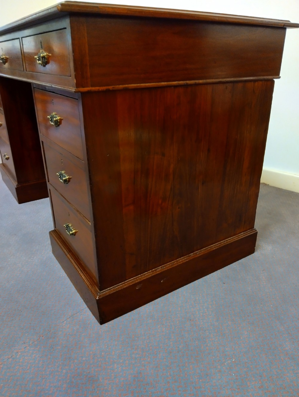 An Edwardian mahogany pedestal desk featuring a brown leather inset writing surface, nine drawers, and brass handles. View V