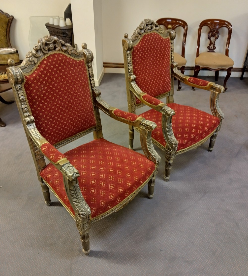 A pair of carved giltwood high-back armchairs upholstered in red patterned fabric with padded armrests and turned legs.