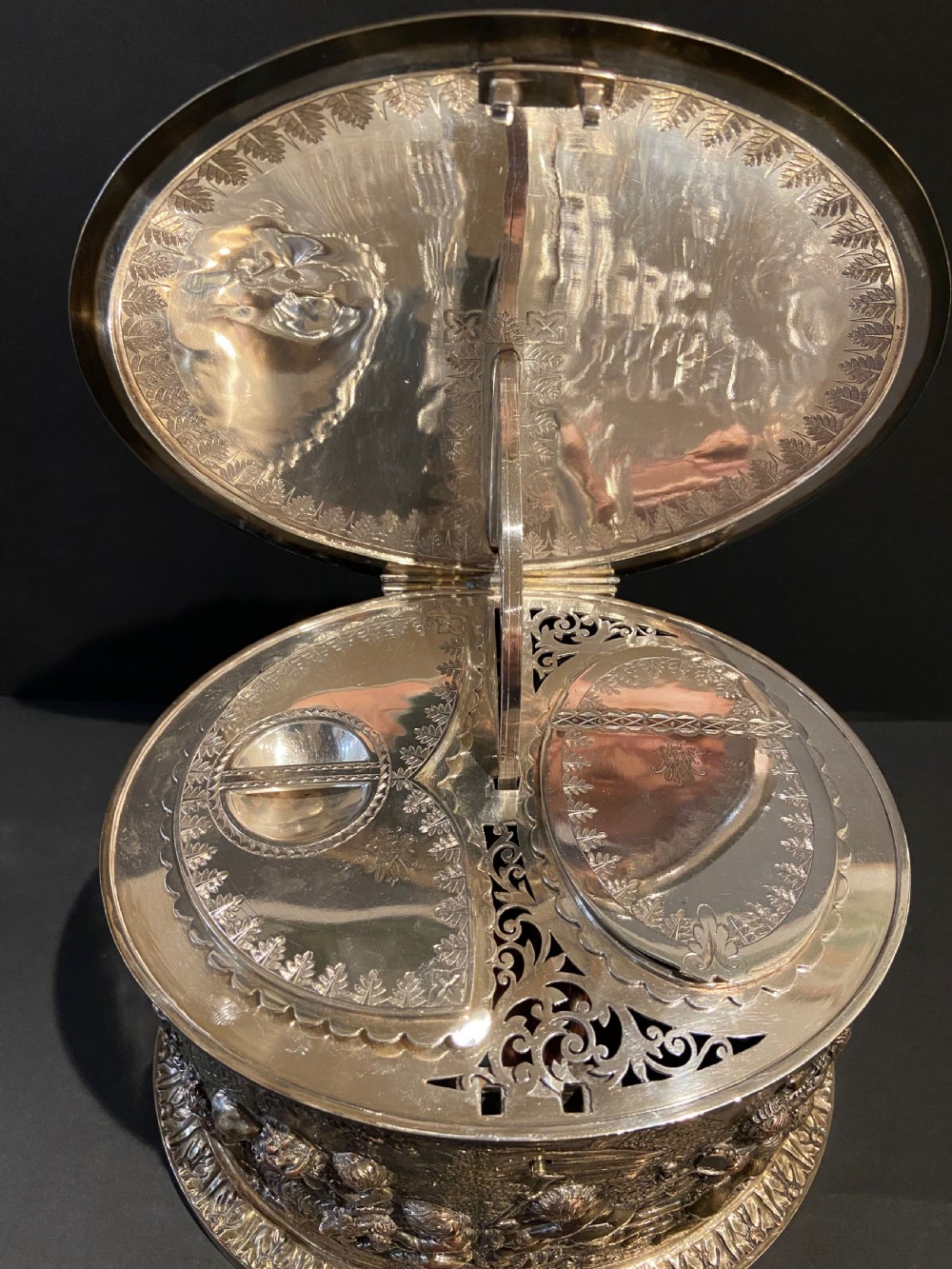 An oval silver-plated tea caddy decorated with high-relief raised figures of cherubs in a landscape setting with gadrooned trim around the base and lid. View V
