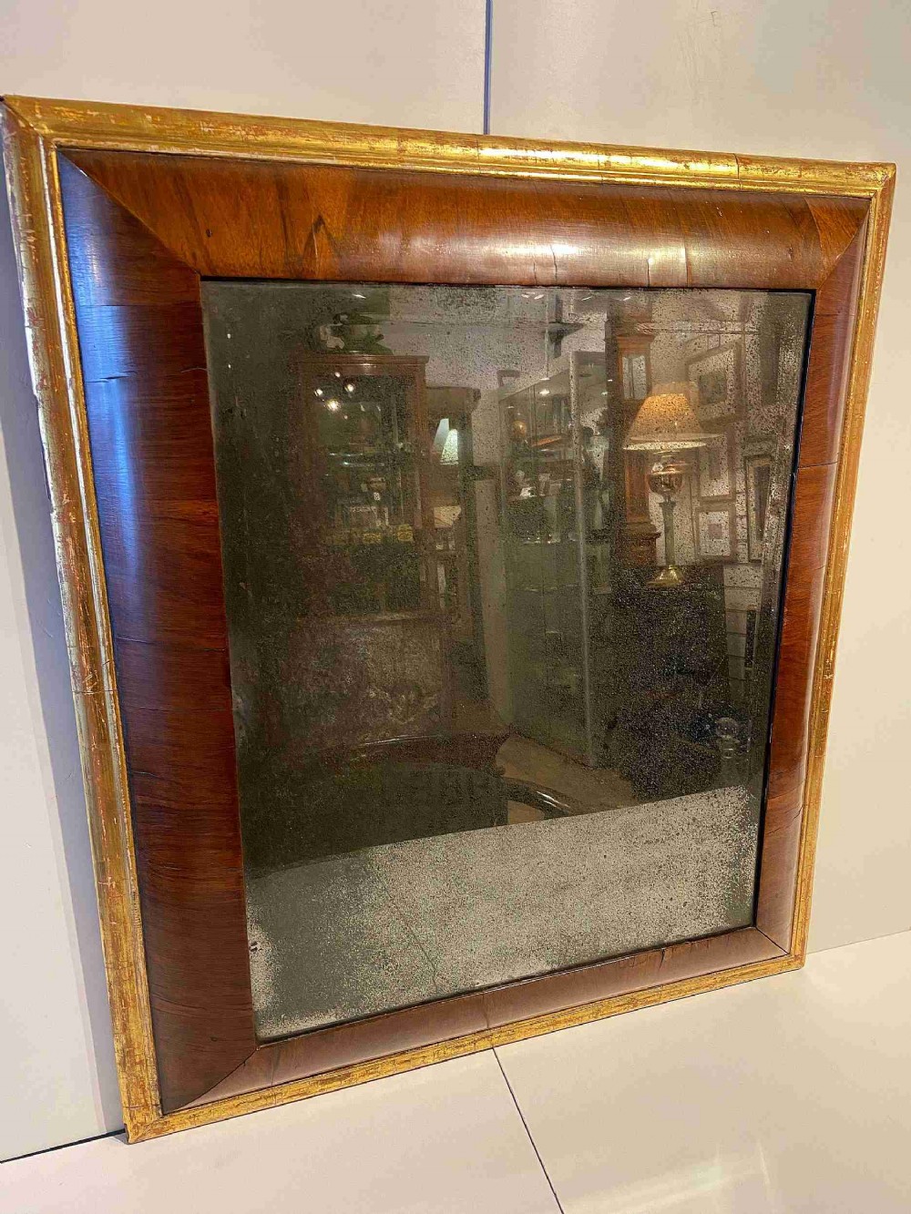 A rectangular Queen Anne period wall mirror featuring a broad convex timber frame with gilt edging and a foxed glass plate.