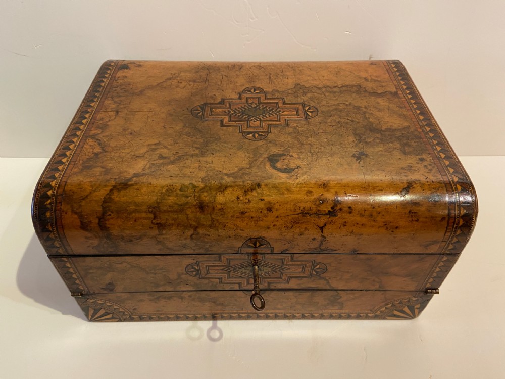 A 19th-century burr walnut box with geometric wood inlay borders, a central star medallion, and a metal key in the front keyhole.
