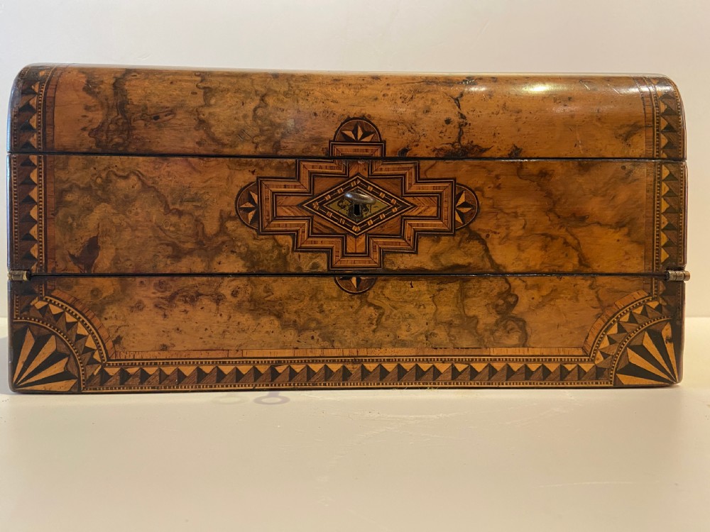 A 19th-century burr walnut box with geometric wood inlay borders, a central star medallion, and a metal key in the front keyhole. View V