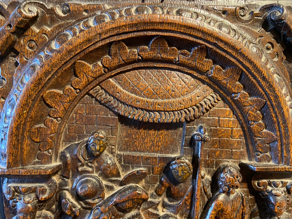 A 16th-century dark oak carved wood panel featuring a high-relief biblical scene enclosed within an arched frame supported by carved side columns. View V