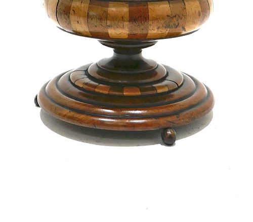 A turned antique wooden lidded tobacco jar with staved bands of light and dark timber, set on a pedestal base with small ball feet. View V