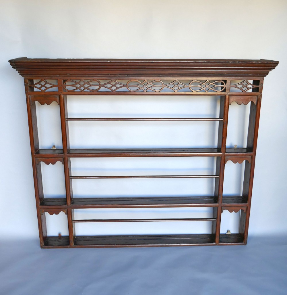 An 18th-century dark pine delft rack with a pierced fretwork frieze, a moulded cornice, three central plate shelves with retention bars, and open side alcoves.