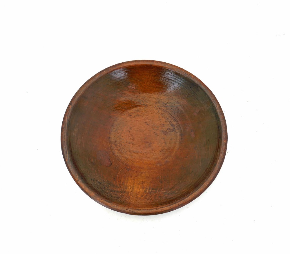 An overhead view of a circular, shallow antique fruitwood bowl showing visible grain and a warm brown patina. View II