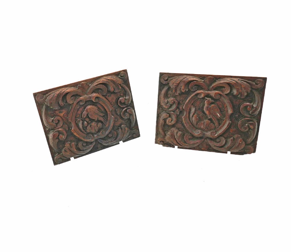 Two rectangular seventeenth-century dark oak panels featuring deep relief carvings of birds surrounded by scrolling floral foliage.