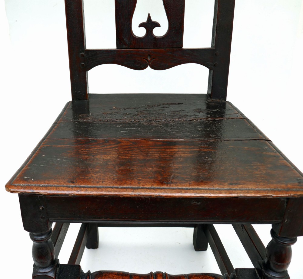 A late 17th-century dark oak side chair featuring a carved cresting rail, a pierced central splat back, turned legs, and a tapestry seat cushion with tassel fringe. View VI