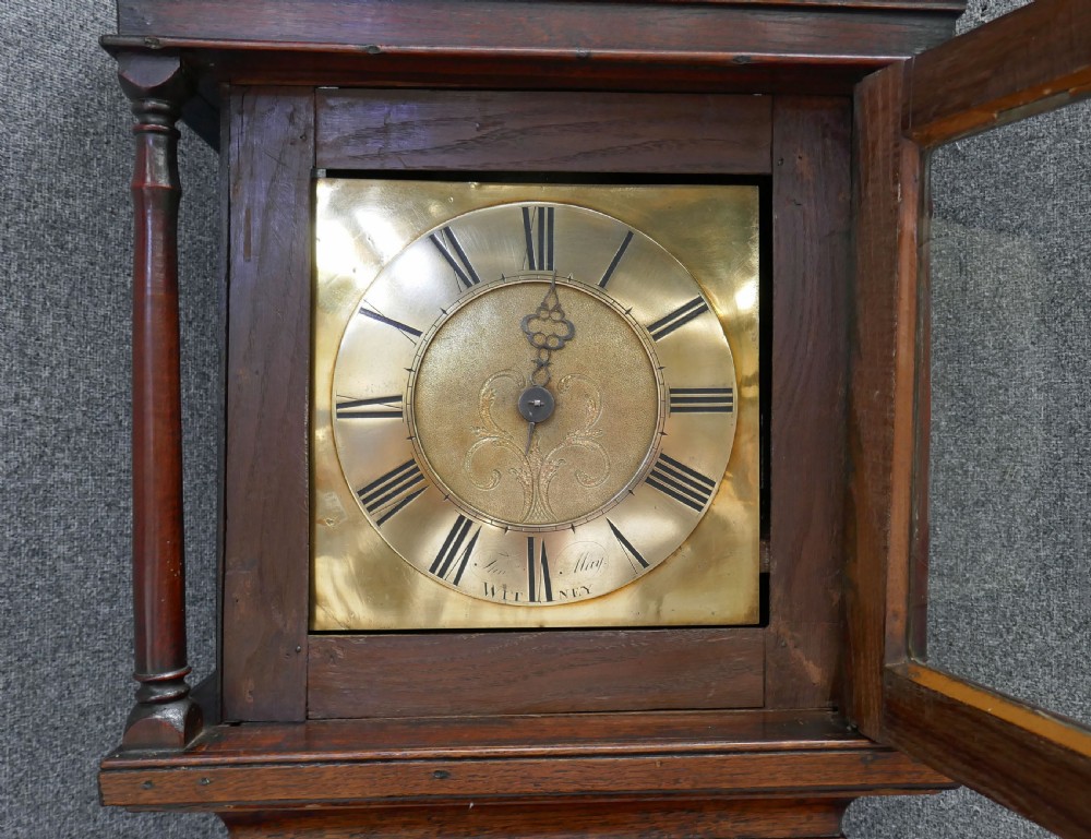 An eighteenth-century Georgian oak longcase clock with a square brass dial, single hand, pediment hood, and simple column details. View II