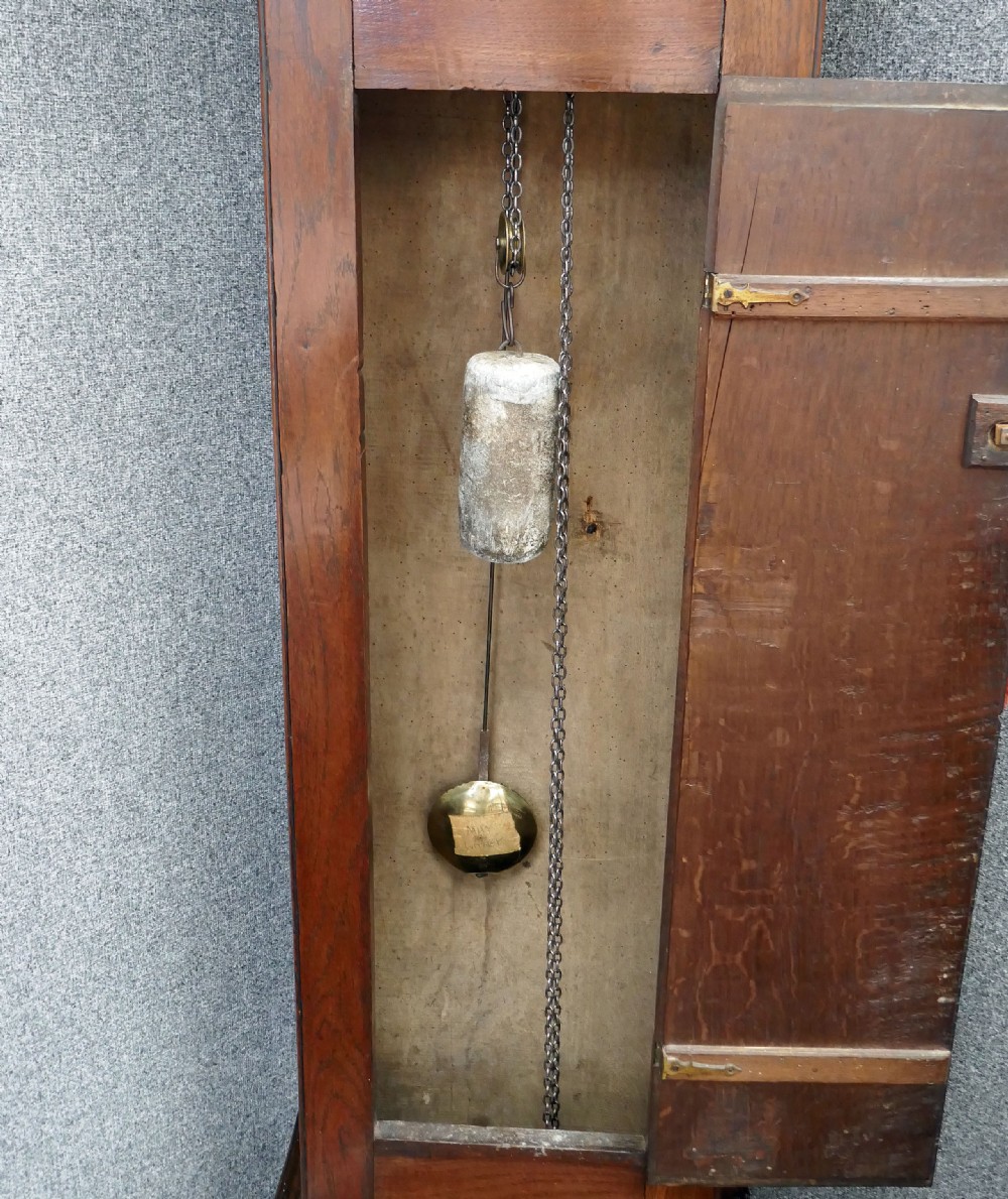 An eighteenth-century Georgian oak longcase clock with a square brass dial, single hand, pediment hood, and simple column details. View III