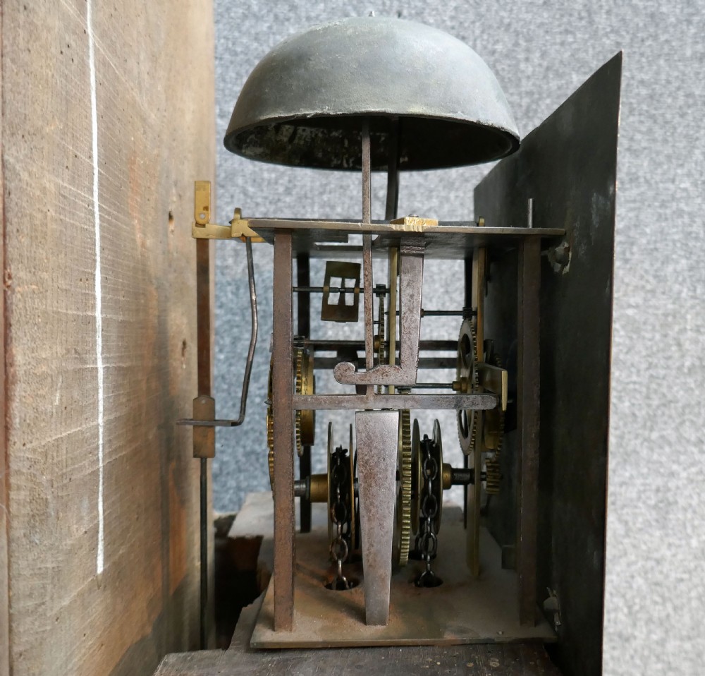 An eighteenth-century Georgian oak longcase clock with a square brass dial, single hand, pediment hood, and simple column details. View V