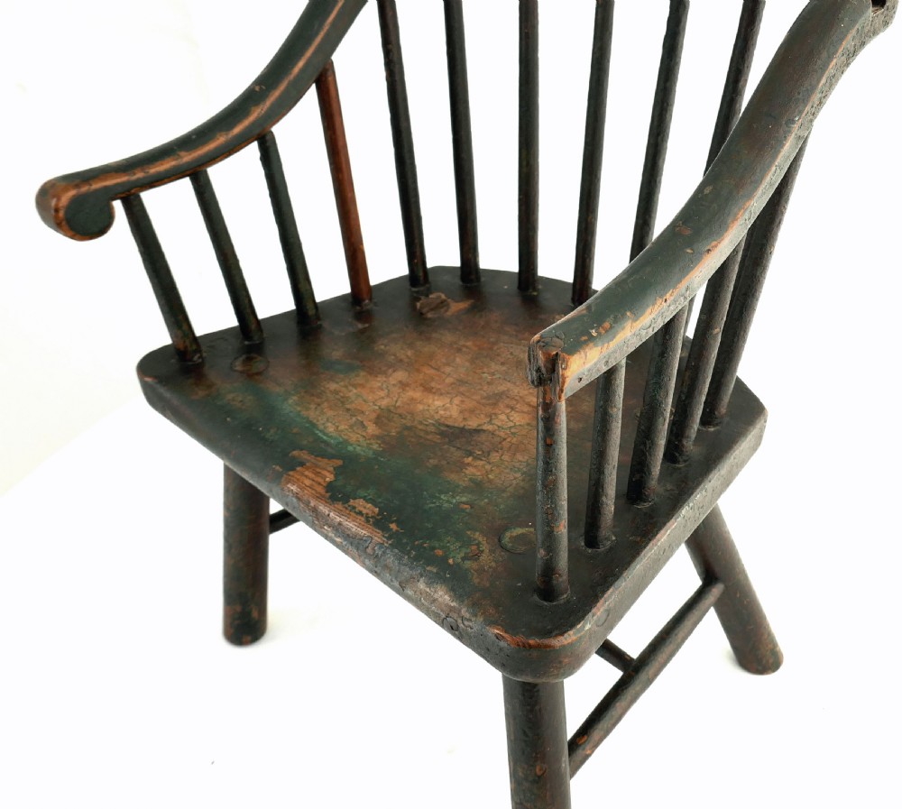 An 18th-century childs stick chair featuring a curved continuous armrest, vertical back spindles, and a distressed dark green painted finish over natural wood. View V