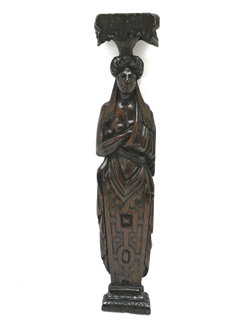 A dark seventeenth-century carved oak caryatid figure depicting a woman with crossed arms on a geometric strapwork base.