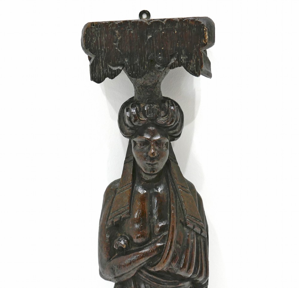 A dark seventeenth-century carved oak caryatid figure depicting a woman with crossed arms on a geometric strapwork base. View II