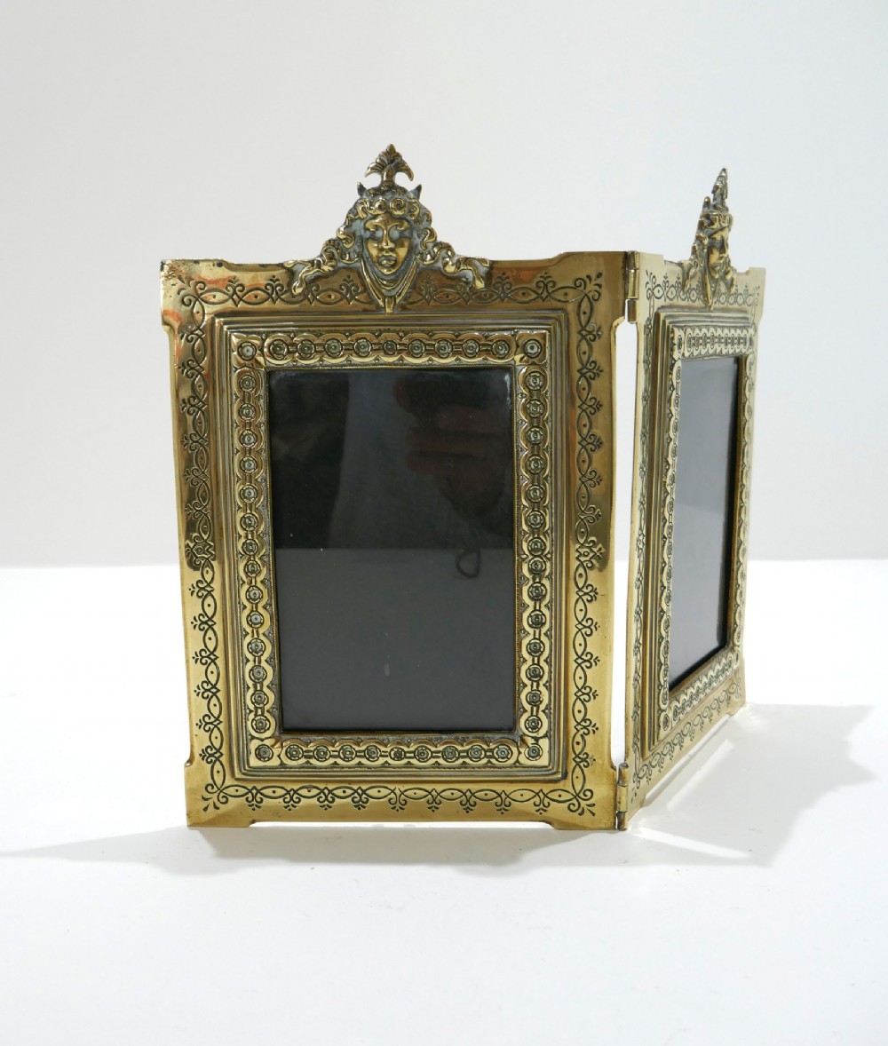 A late 19th-century Victorian double brass picture frame with ornate engraved geometric borders and classical mask finials. View II