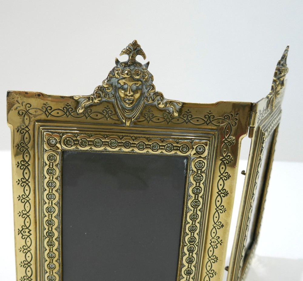 A late 19th-century Victorian double brass picture frame with ornate engraved geometric borders and classical mask finials. View III