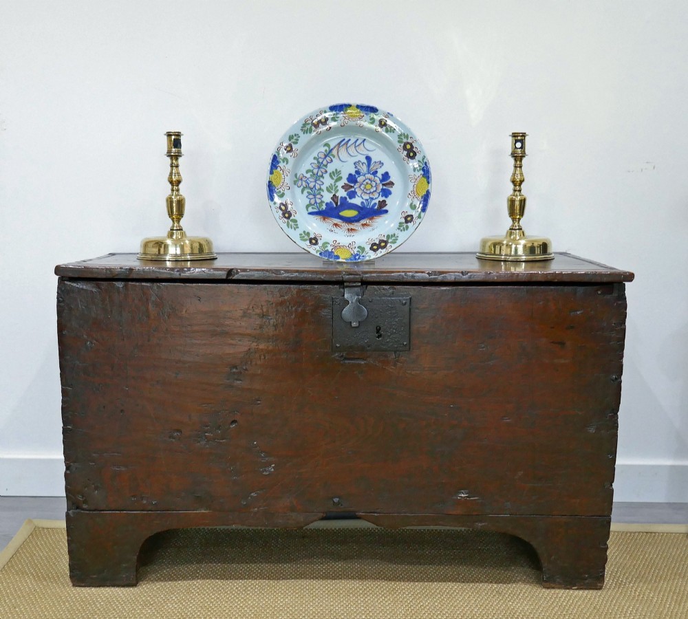 A sixteenth-century dark oak boarded coffer featuring a simple flat lid, an iron lockplate on the front panel, and a shaped lower apron.