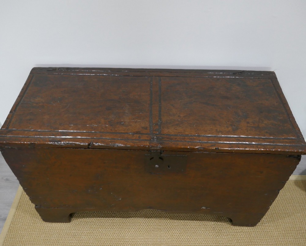 A sixteenth-century dark oak boarded coffer featuring a simple flat lid, an iron lockplate on the front panel, and a shaped lower apron. View IV