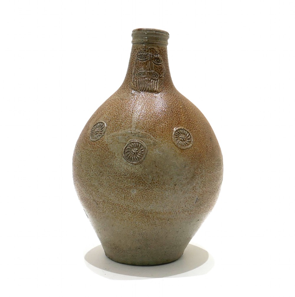 A 17th-century bulbous brown salt-glazed stoneware Bellarmine jug featuring a relief-carved bearded mask on the neck and decorative rosette medallions.
