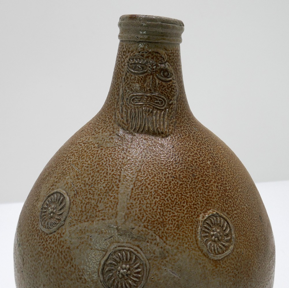 A 17th-century bulbous brown salt-glazed stoneware Bellarmine jug featuring a relief-carved bearded mask on the neck and decorative rosette medallions. View II