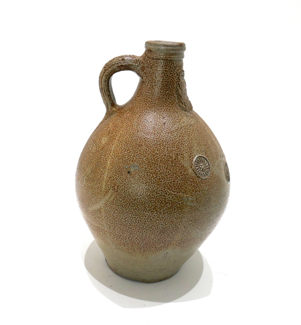 A 17th-century bulbous brown salt-glazed stoneware Bellarmine jug featuring a relief-carved bearded mask on the neck and decorative rosette medallions. View III