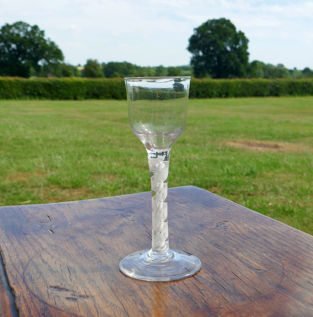 An eighteenth-century clear lead glass wine glass featuring an ogee bowl, an opaque white twist stem, and a conical foot.