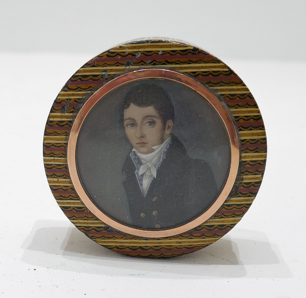 A circular 19th-century lacquered treen snuff box featuring a central hand-painted miniature portrait of a young man surrounded by a gold frame and patterned border.