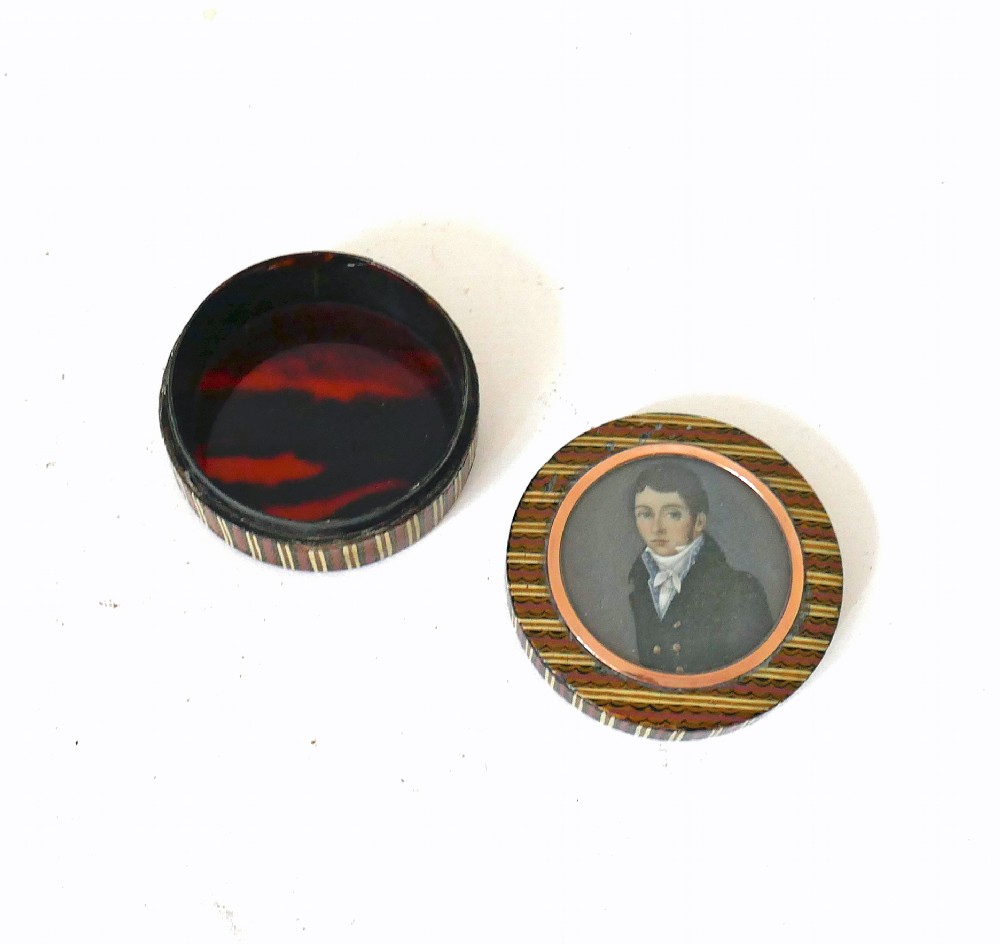 A circular 19th-century lacquered treen snuff box featuring a central hand-painted miniature portrait of a young man surrounded by a gold frame and patterned border. View II