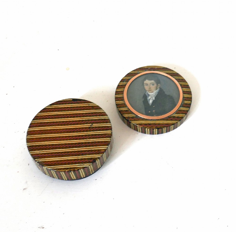 A circular 19th-century lacquered treen snuff box featuring a central hand-painted miniature portrait of a young man surrounded by a gold frame and patterned border. View IV