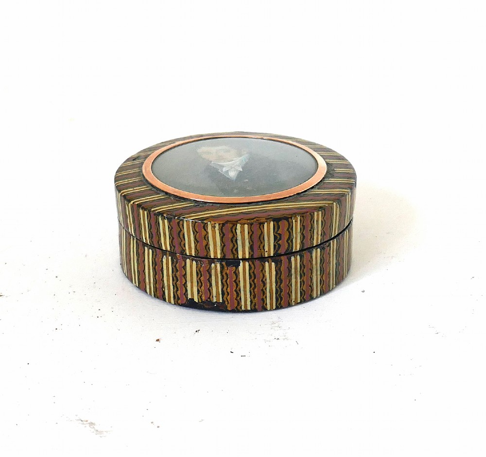 A circular 19th-century lacquered treen snuff box featuring a central hand-painted miniature portrait of a young man surrounded by a gold frame and patterned border. View V