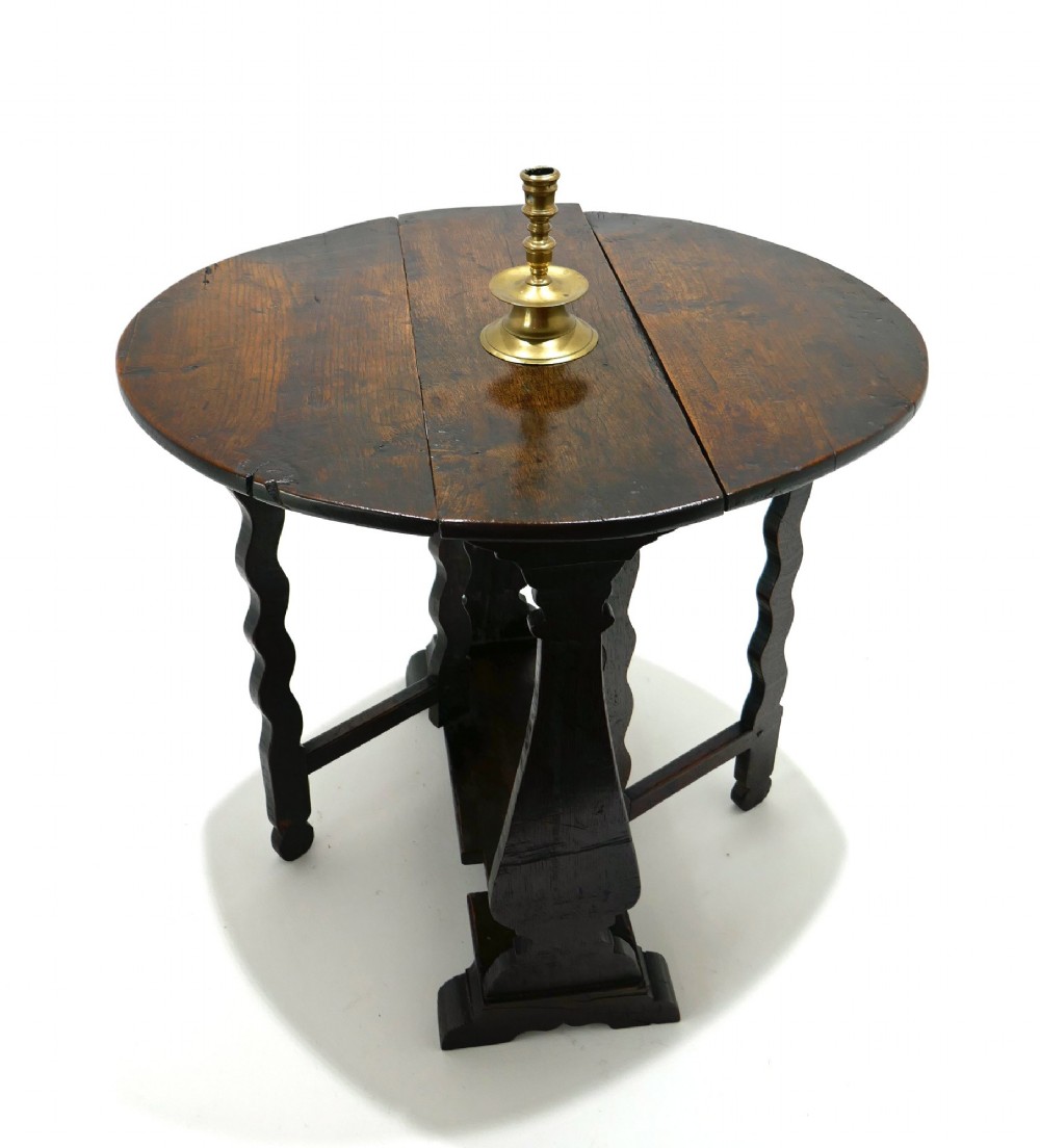 A seventeenth-century English dark oak gateleg table featuring a rounded drop-leaf top supported by shaped gates and trestle feet.