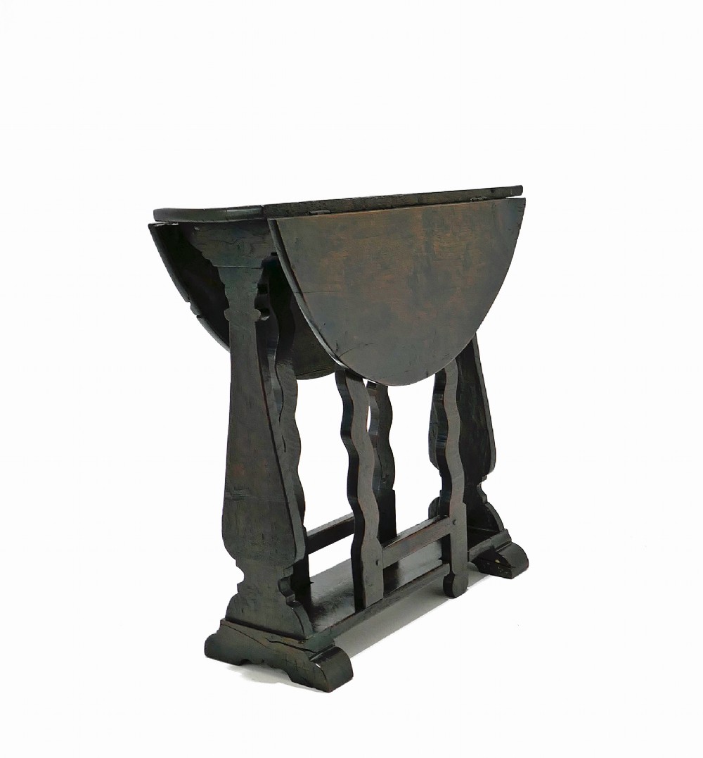 A seventeenth-century English dark oak gateleg table featuring a rounded drop-leaf top supported by shaped gates and trestle feet. View III