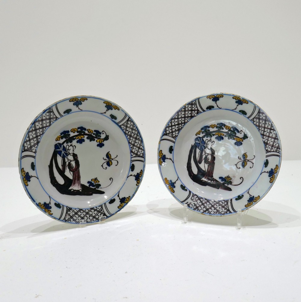A pair of 18th-century circular tin-glazed earthenware plates decorated with hand-painted polychrome chinoiserie figures and floral rim borders.