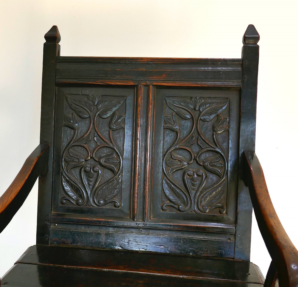 A 17th-century dark oak wainscot chair with carved floral back panels, turned front legs, and wooden perimeter stretchers. View II