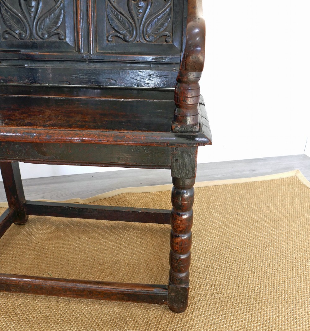 A 17th-century dark oak wainscot chair with carved floral back panels, turned front legs, and wooden perimeter stretchers. View III