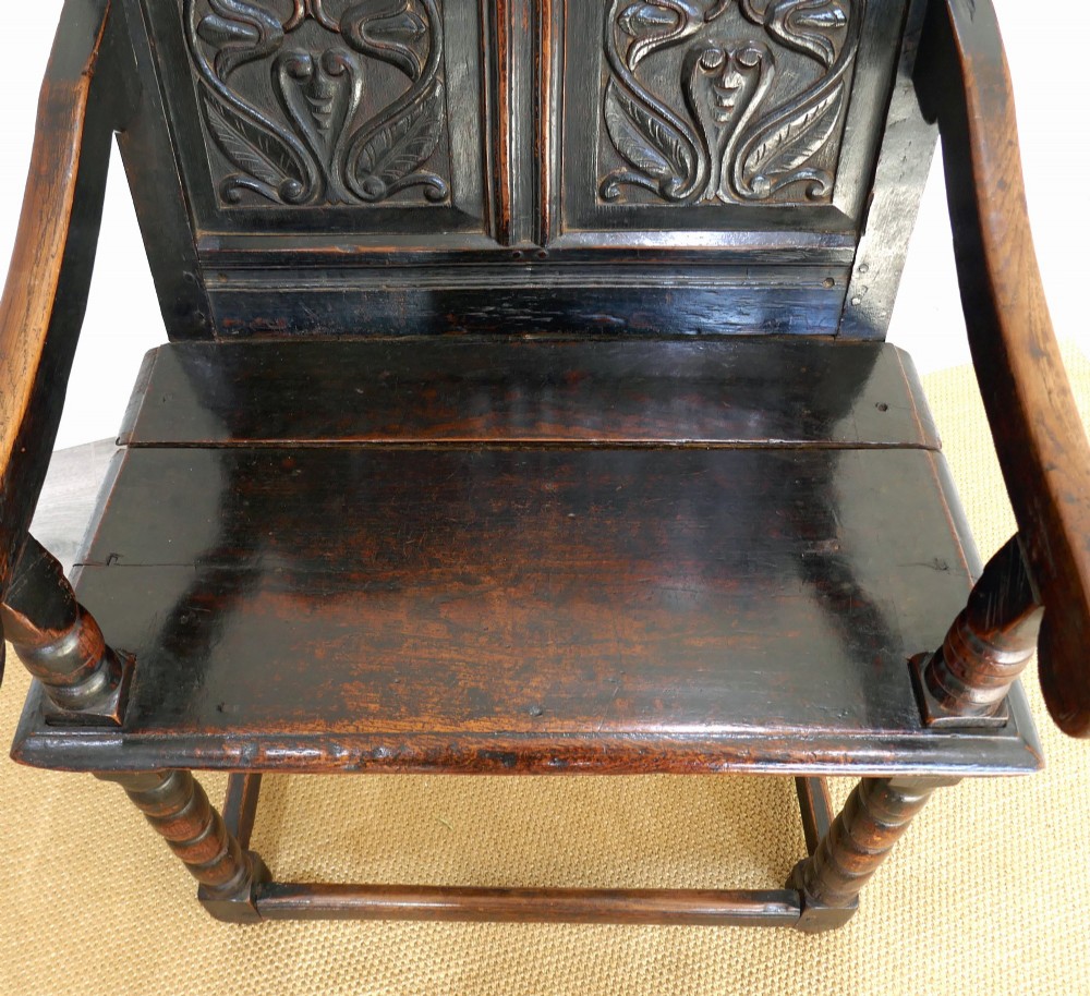 A 17th-century dark oak wainscot chair with carved floral back panels, turned front legs, and wooden perimeter stretchers. View IV