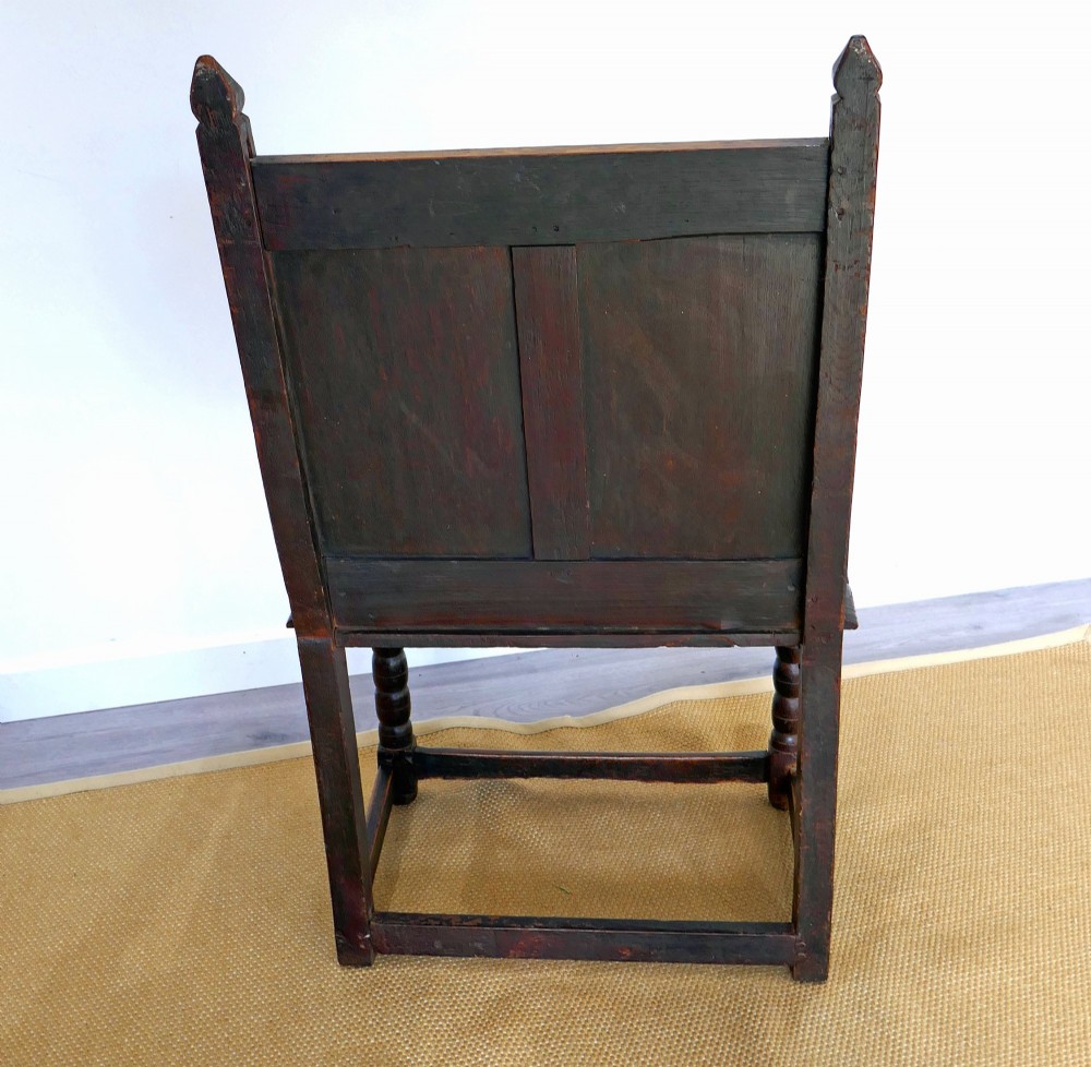 A 17th-century dark oak wainscot chair with carved floral back panels, turned front legs, and wooden perimeter stretchers. View VI