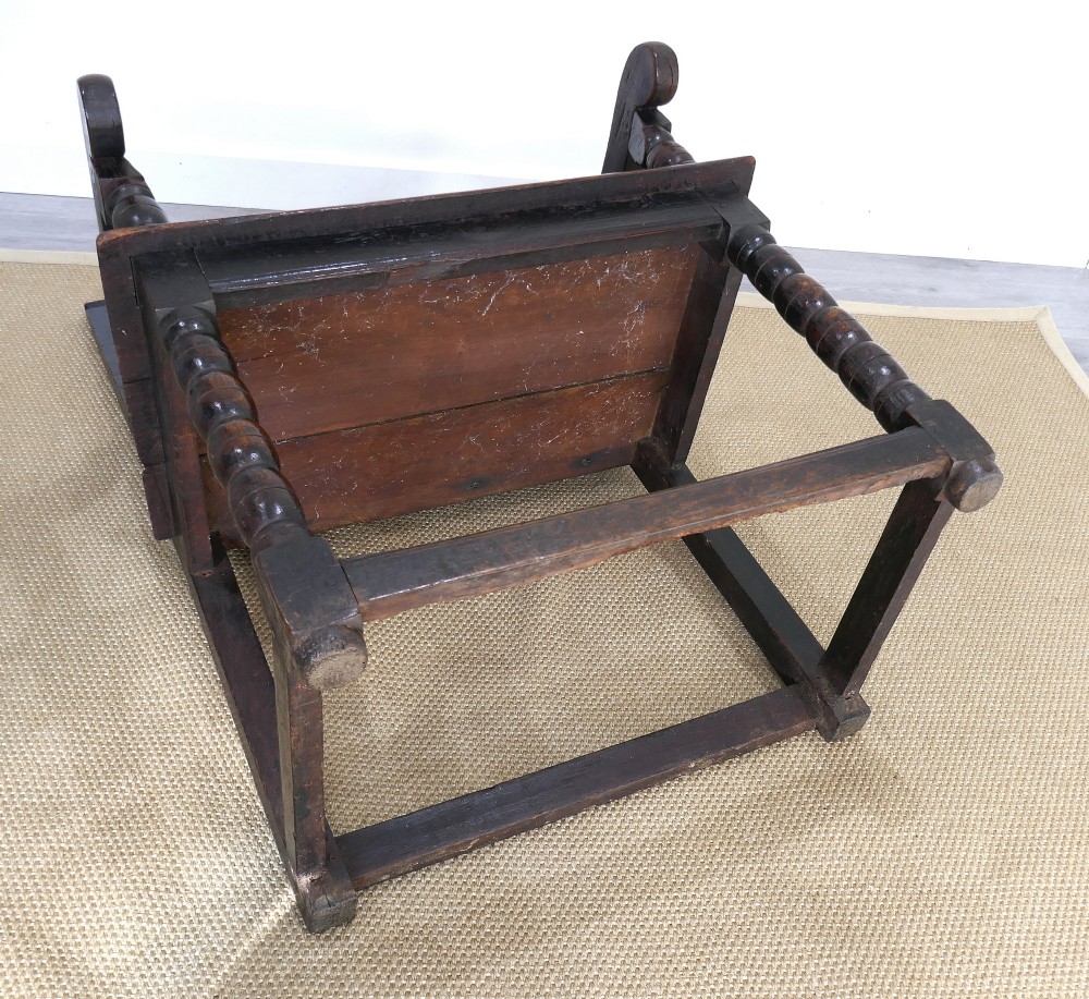 A 17th-century dark oak wainscot chair with carved floral back panels, turned front legs, and wooden perimeter stretchers. View VII