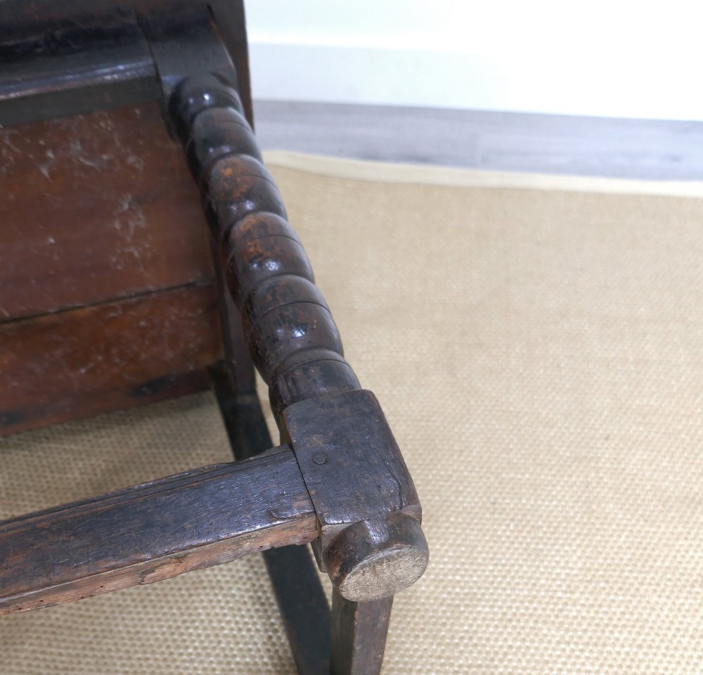 A 17th-century dark oak wainscot chair with carved floral back panels, turned front legs, and wooden perimeter stretchers. View VIII