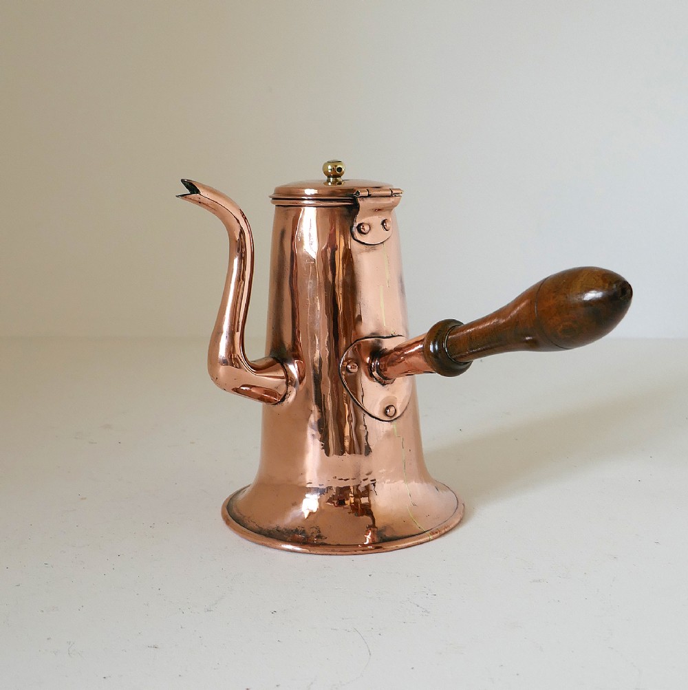 A Georgian copper coffee pot featuring a tapered body, flared base, swan-neck spout, hinged lid with brass finial, and a turned wooden side handle.