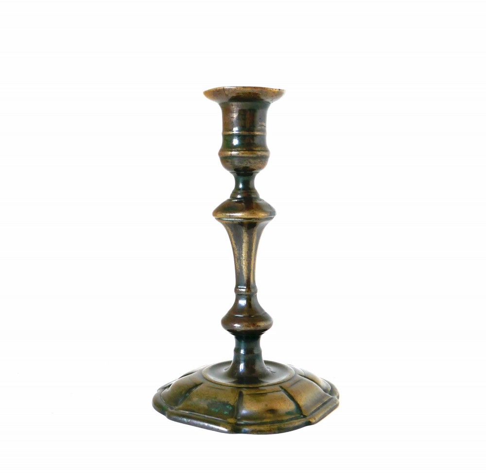 An eighteenth-century cast brass candlestick featuring a baluster stem and a scalloped base with dark surface patina.