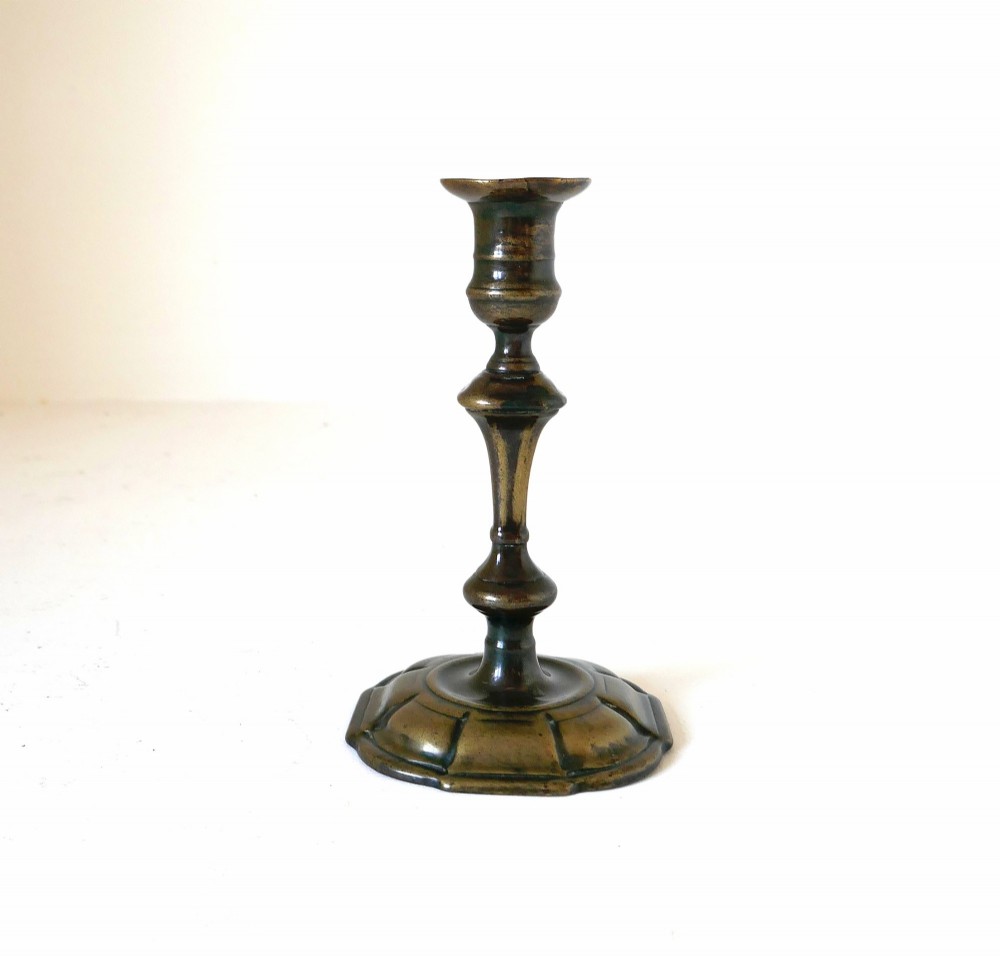 An eighteenth-century cast brass candlestick featuring a baluster stem and a scalloped base with dark surface patina. View II