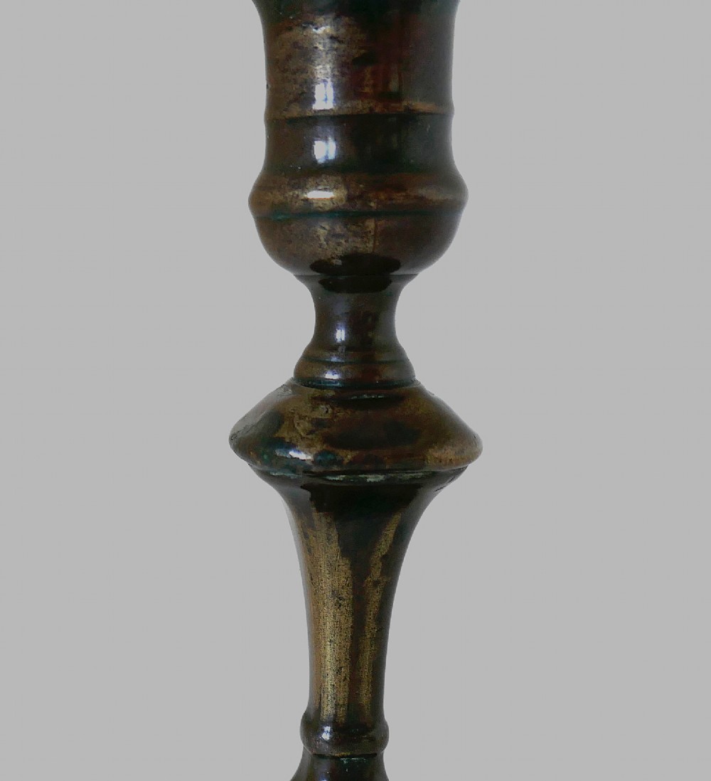 An eighteenth-century cast brass candlestick featuring a baluster stem and a scalloped base with dark surface patina. View V