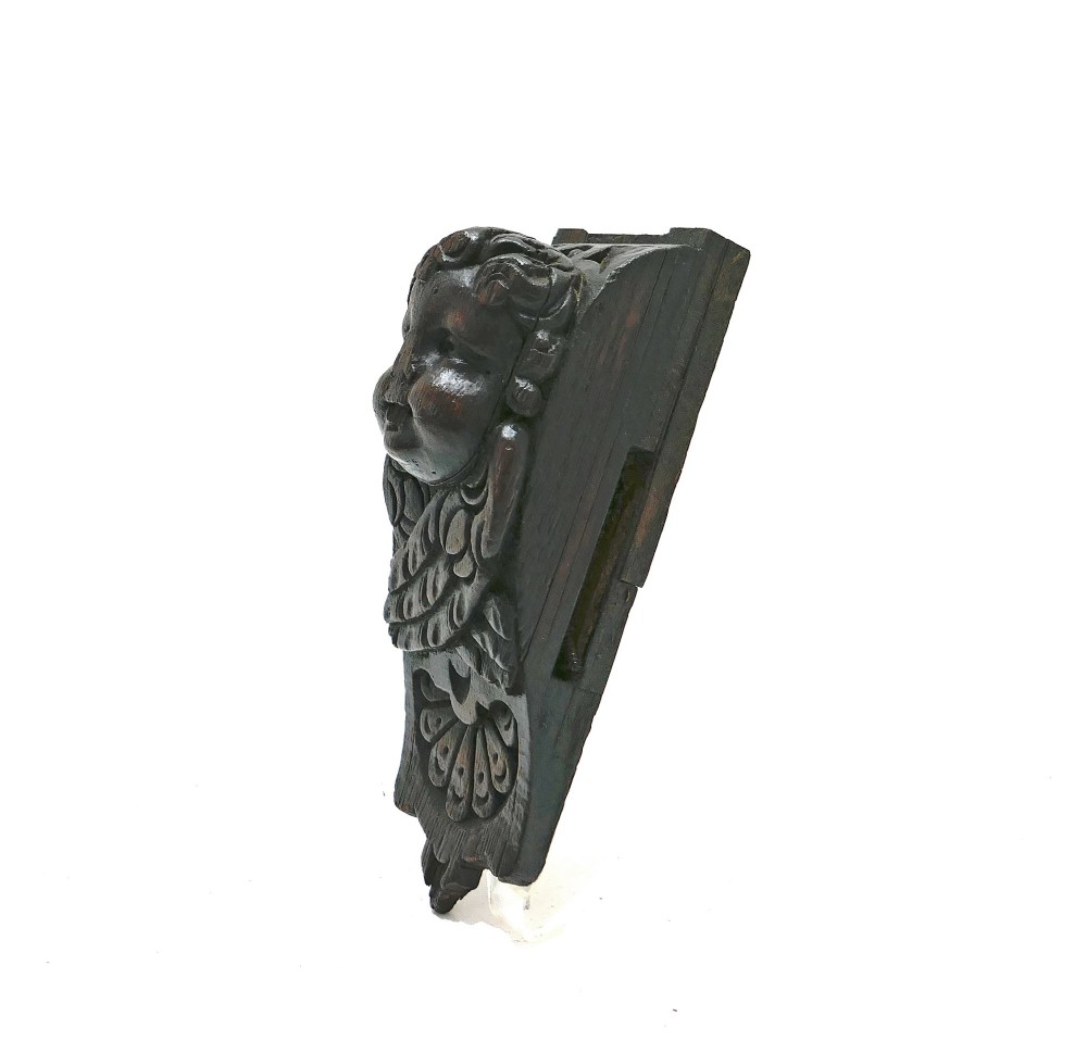 A dark carved oak architectural applique featuring a sculpted cherub head with folded wings and a fan motif at the base. View II